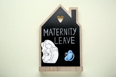 Photo of Maternity leave concept. Wooden house figure, baby pacifier and paper cutout on white background, top view