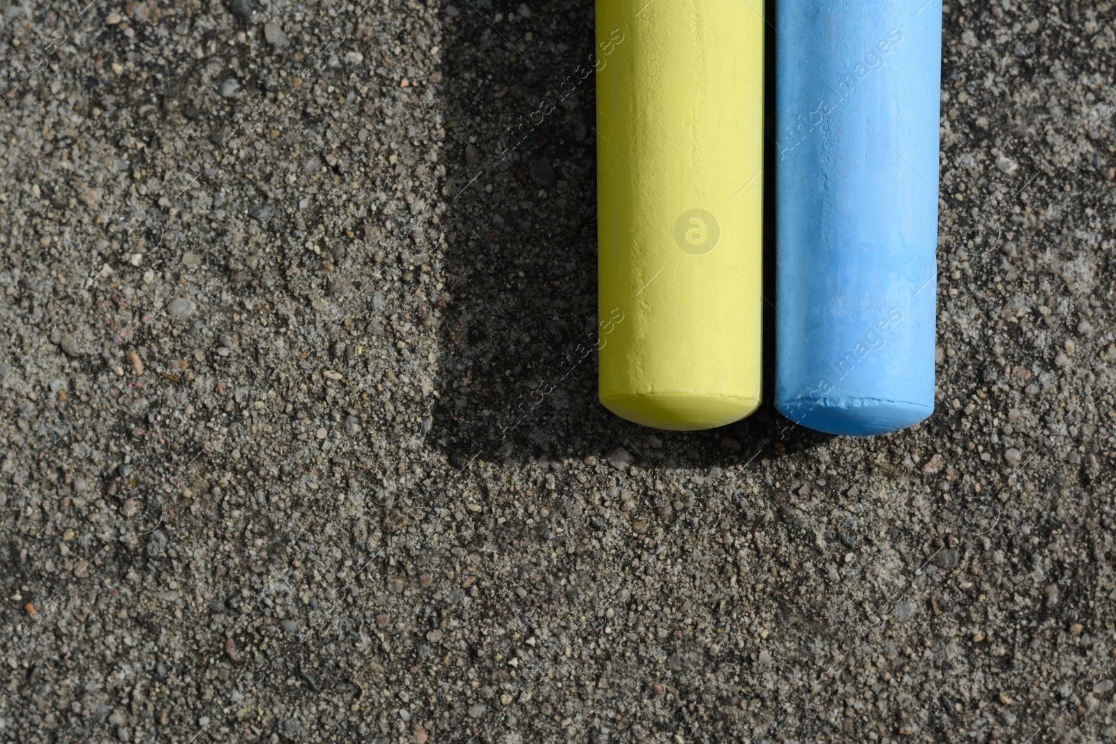 Photo of Yellow and light blue chalk sticks on asphalt, flat lay. Space for text