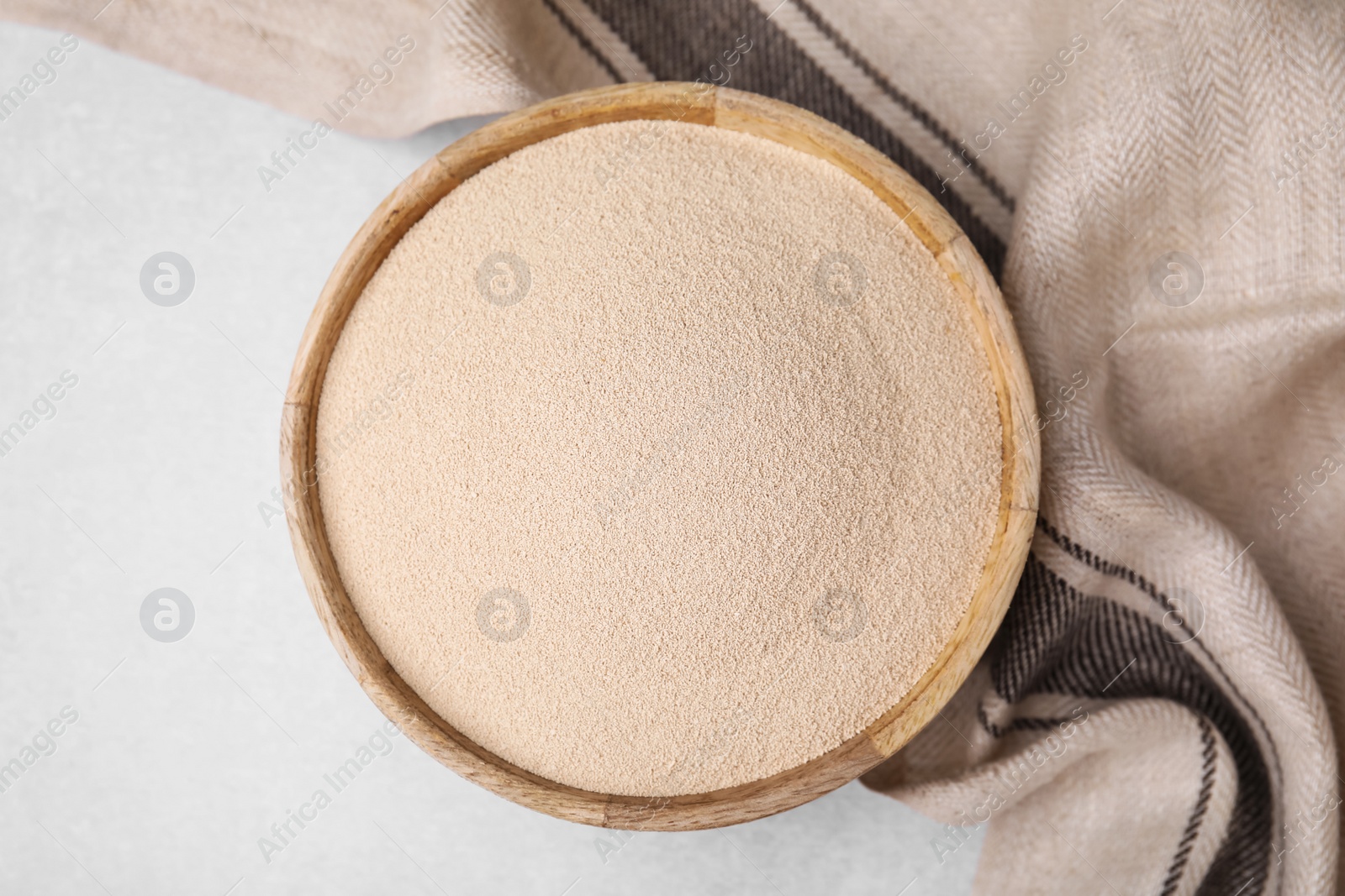 Photo of Granulated yeast in wooden bowl on light gray table, top view