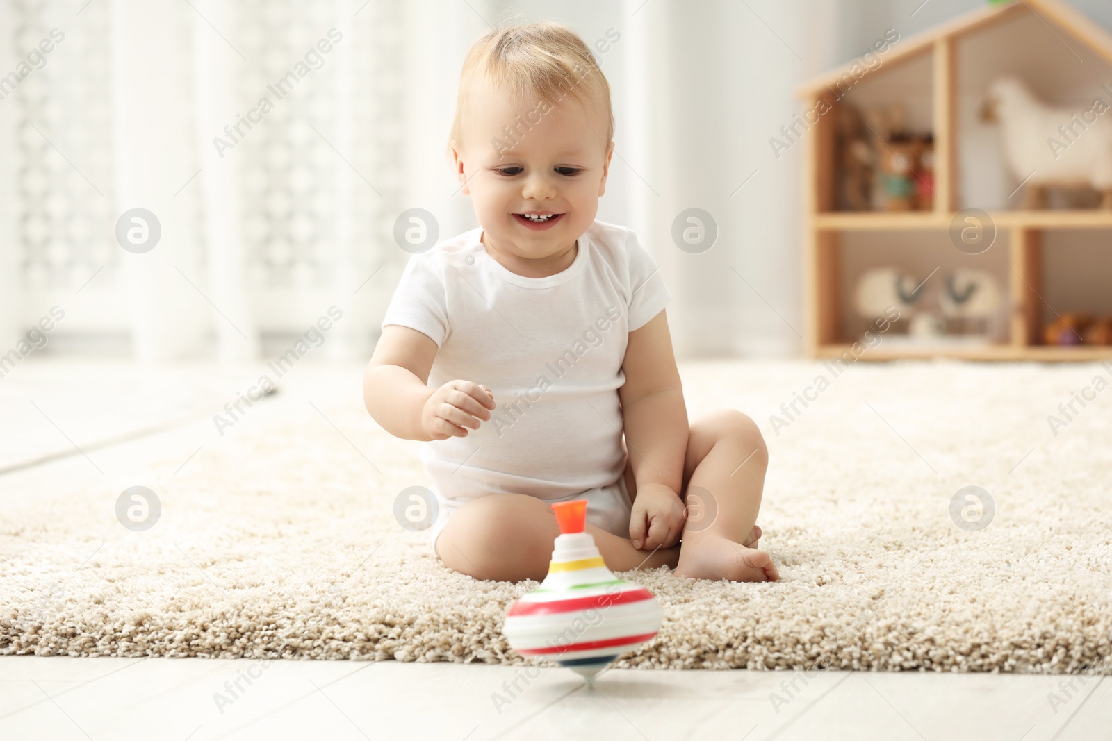 Photo of Children toys. Cute little boy playing with spinning top on rug at home