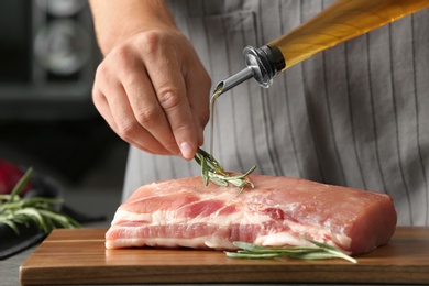 Photo of Man cooking fresh raw meat with oil and rosemary on wooden board, closeup