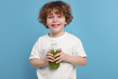 Photo of Cute little boy with glass bottle of fresh juice on light blue background