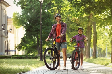 Photo of Dad and son riding bicycles in park on sunny day