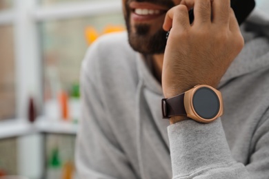 Photo of Happy man wearing smart watch and talking on smartphone indoors, closeup