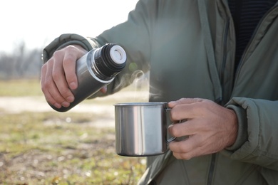 Photo of Man pouring hot drink into mug from thermos outdoors, closeup