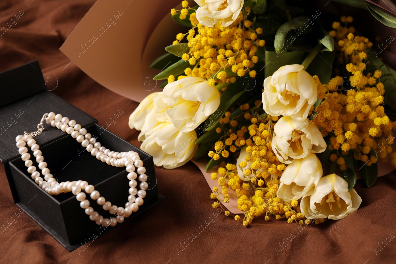 Photo of Bouquet of beautiful spring flowers and necklace on brown fabric, above view