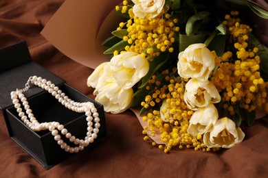 Photo of Bouquet of beautiful spring flowers and necklace on brown fabric, above view