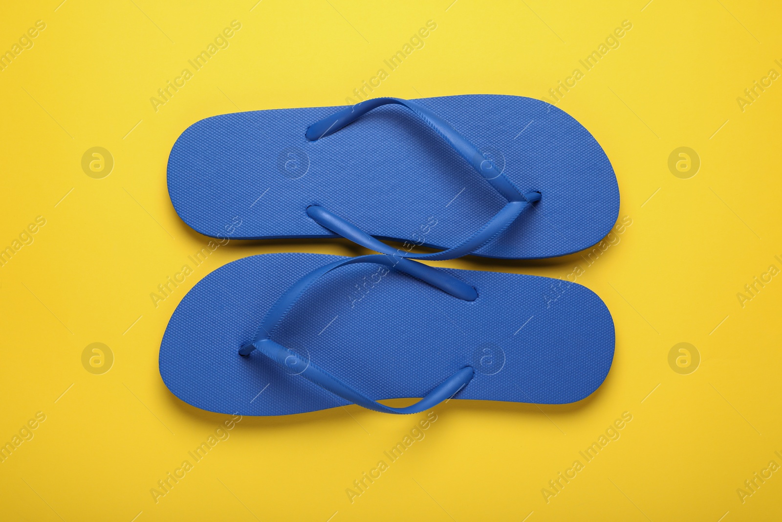 Photo of Stylish blue flip flops on yellow background, top view