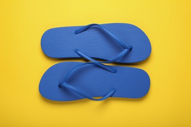 Stylish blue flip flops on yellow background, top view