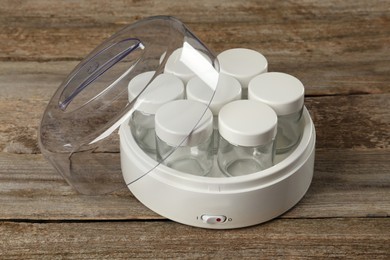 Modern yogurt maker with empty jars on wooden table