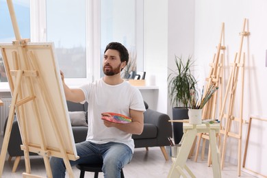 Photo of Man painting in studio. Using easel to hold canvas