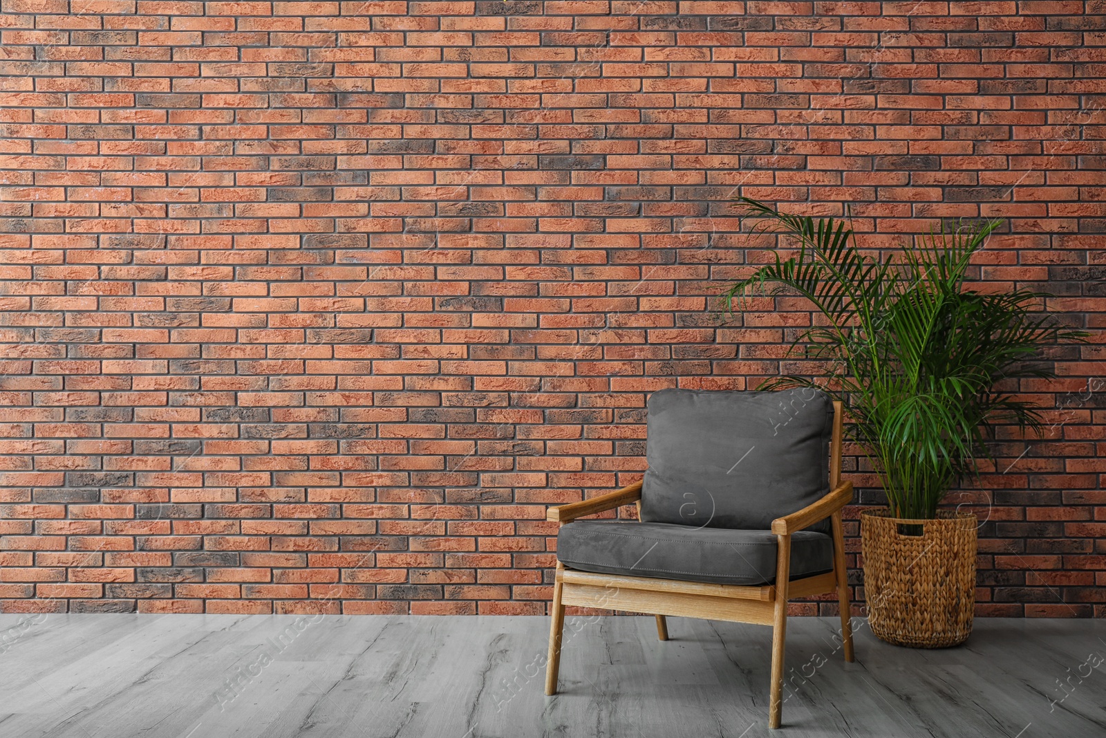 Photo of Modern room interior with stylish grey armchair and potted plant near brick wall