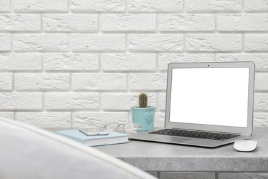 Photo of Laptop on desk against brick wall in home office. Comfortable workplace