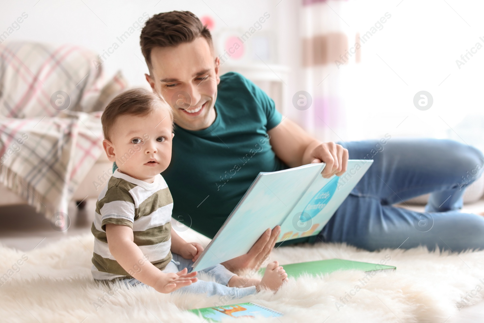 Photo of Young father reading book with his cute little son at home