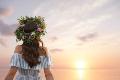 Photo of Young woman wearing wreath made of beautiful flowers near river, back view