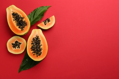 Fresh ripe papaya fruits with green leaves on red background, flat lay. Space for text