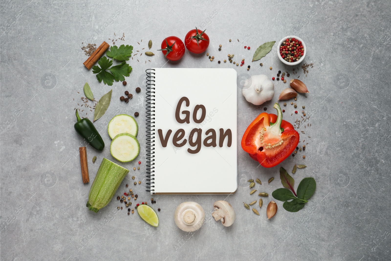 Image of Notebook with phrase Go Vegan, fresh vegetables and spices on light grey background, flat lay