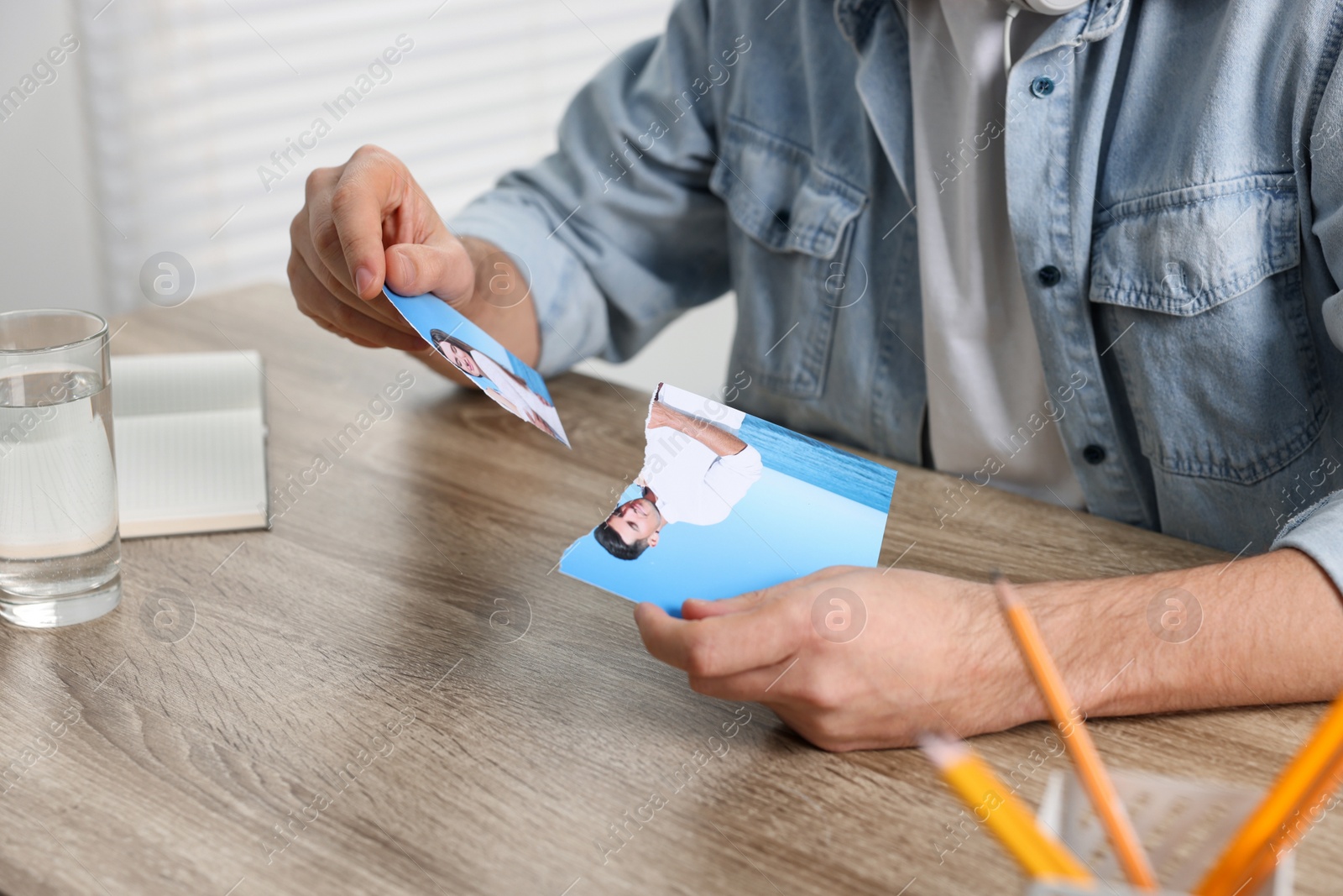 Photo of Man holding parts of photo at table indoors, closeup. Divorce concept