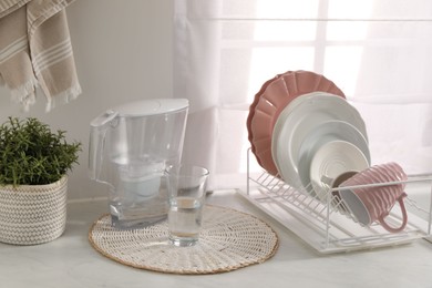 Drainer with different clean dishware, cup, glass and filter jug on light table indoors