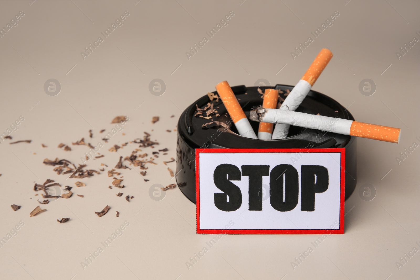 Photo of Card with word Stop, ashtray and cigarette stubs on beige background, closeup with space for text. Quitting smoking concept