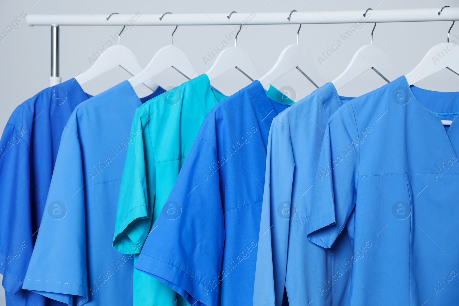 Photo of Different medical uniforms on rack against light grey background