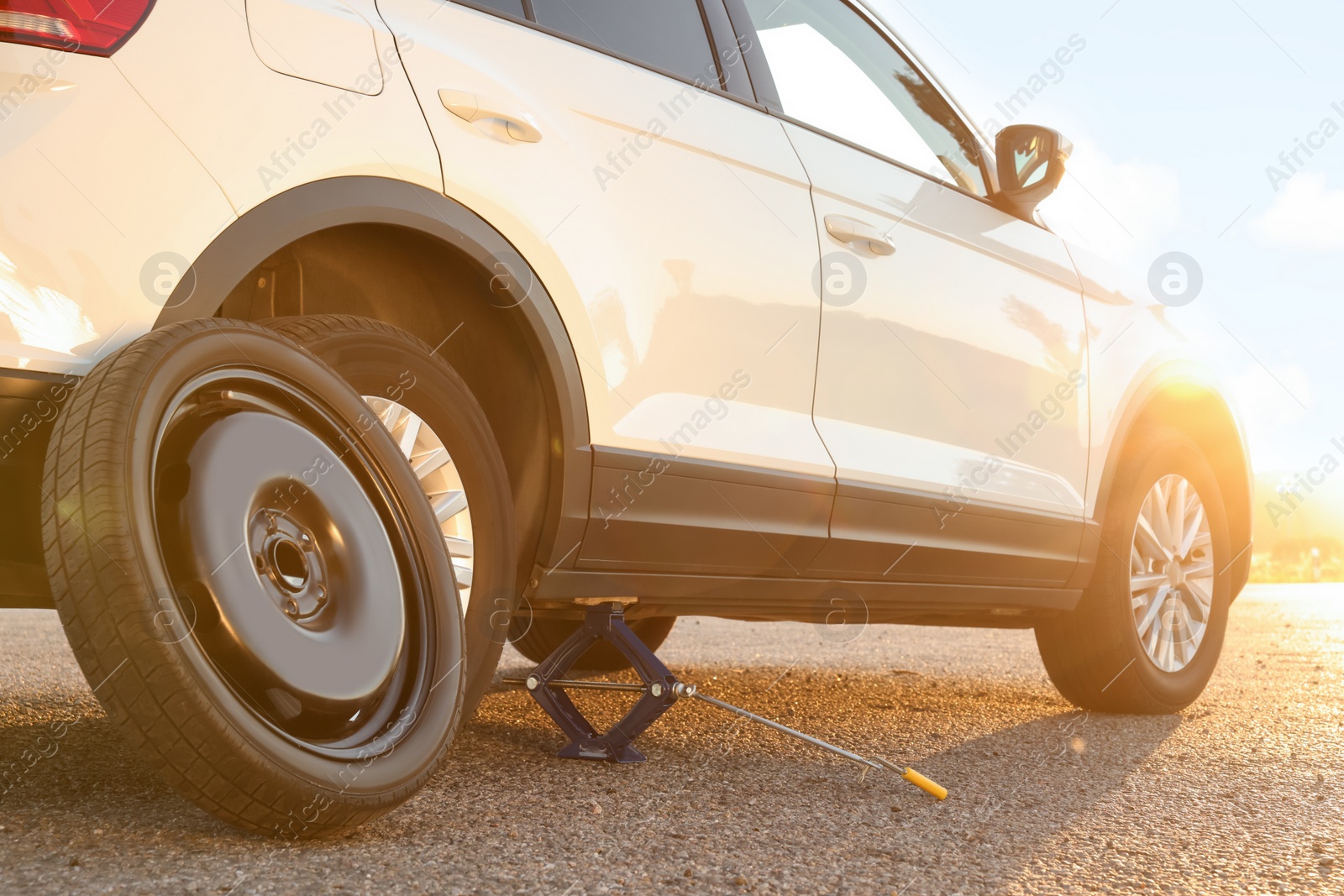 Photo of Car lifted by scissor jack and spare wheel on roadside