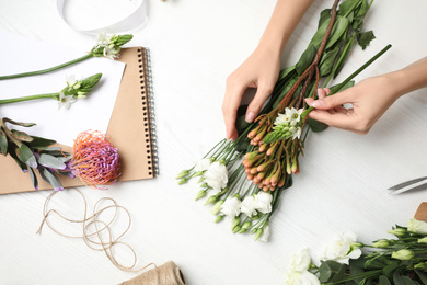 Florist making beautiful bouquet at white wooden table, top view