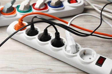 Photo of Power strip with extension cords on white wooden floor, closeup. Electrician's equipment