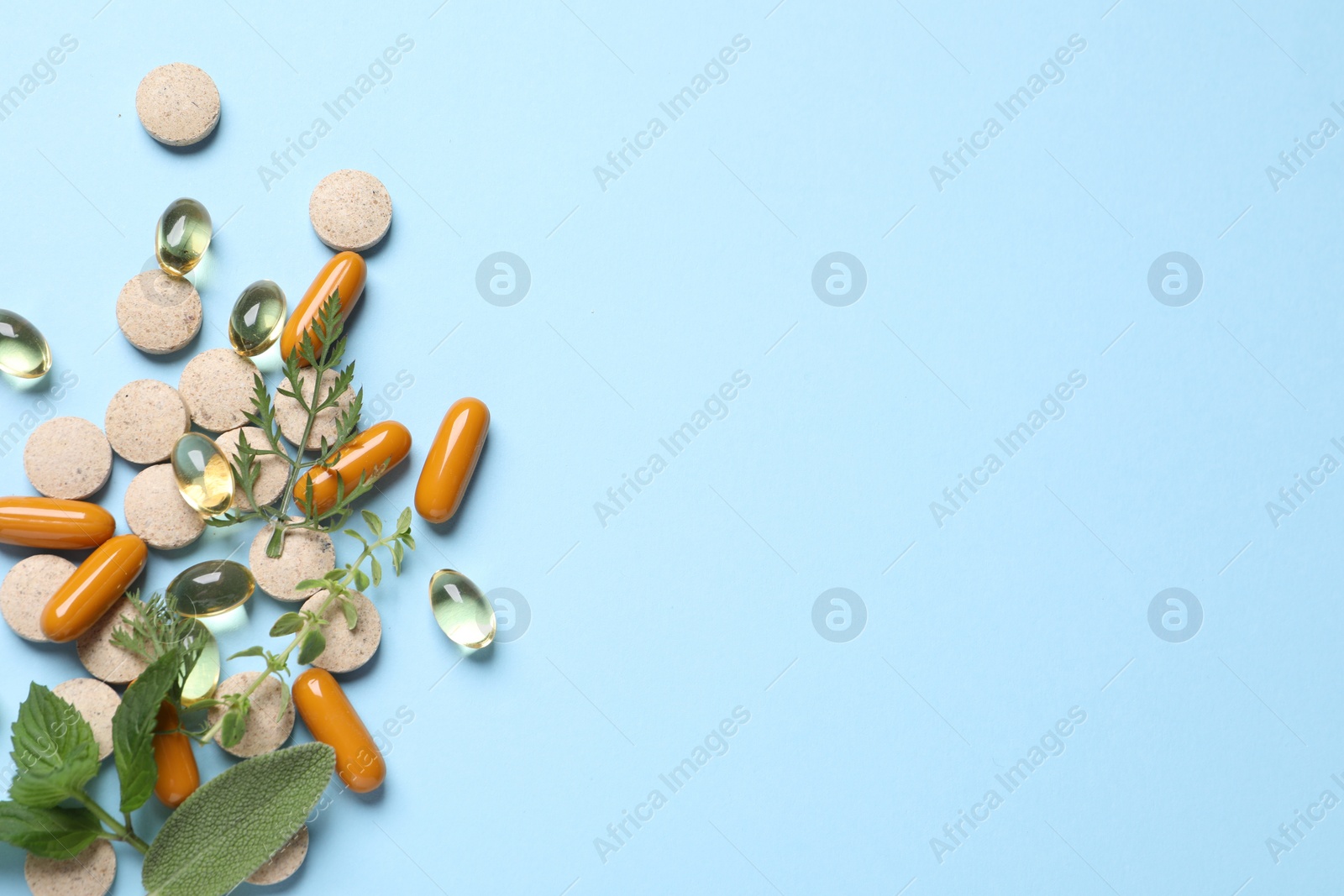 Photo of Different pills and herbs on light blue background, flat lay with space for text. Dietary supplements