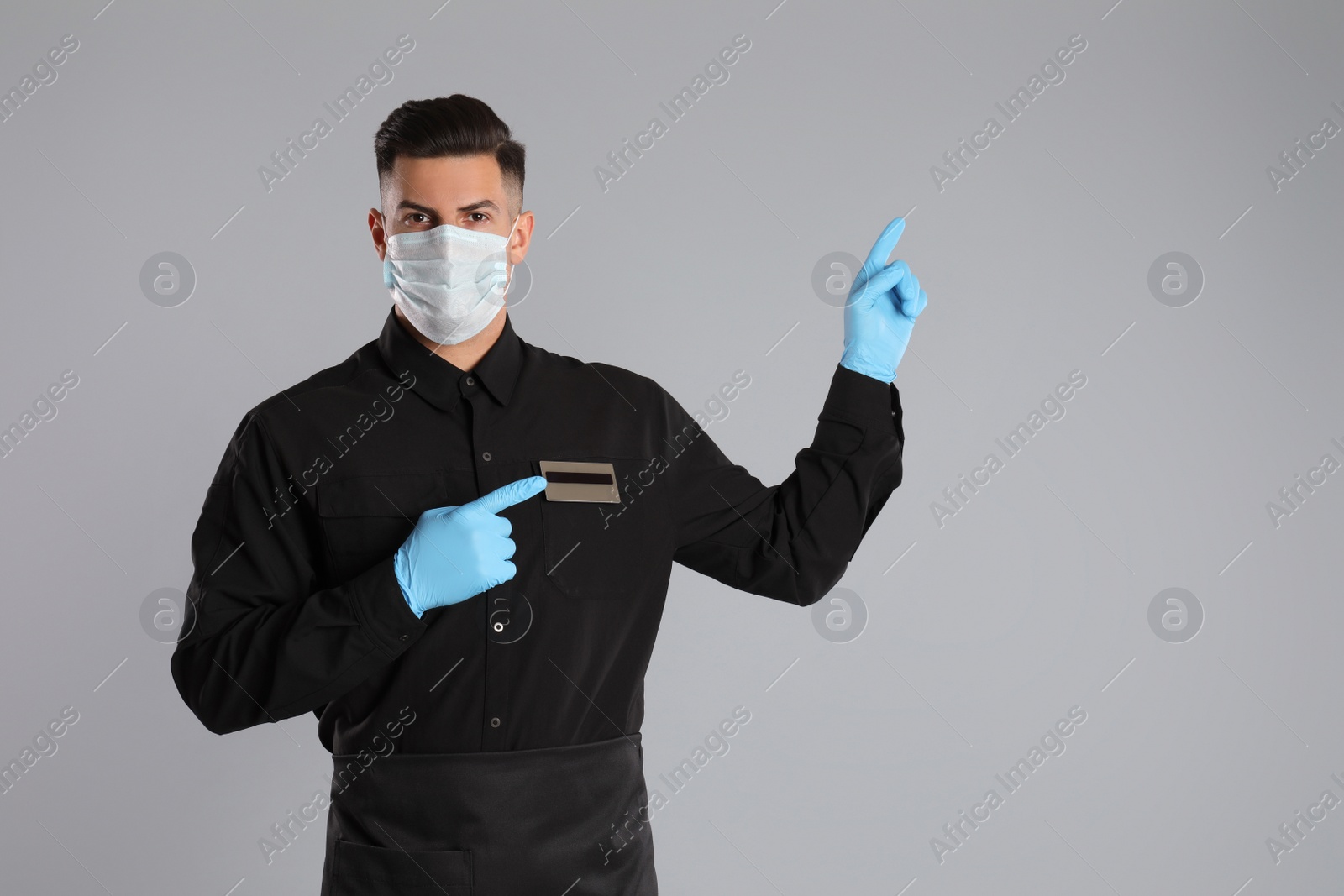 Photo of Waiter wearing medical face mask on light grey background