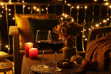 Photo of Glasses of wine, burning candles and decor on rattan table. Autumn evening on terrace