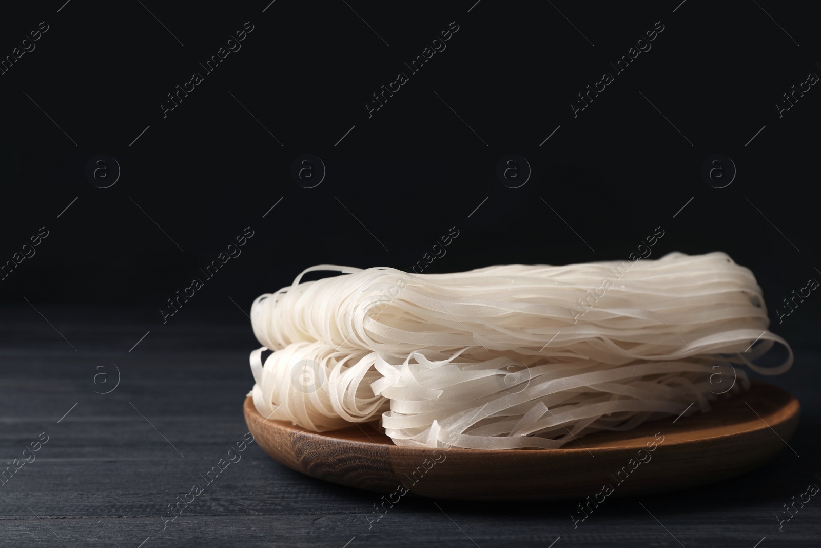 Photo of Plate with raw rice noodles on wooden table. Space for text