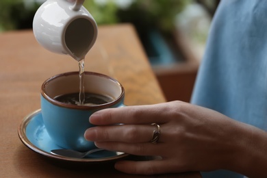 Photo of Woman adding water to fresh aromatic coffee at table, closeup