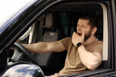 Photo of Tired man yawning while driving his modern car