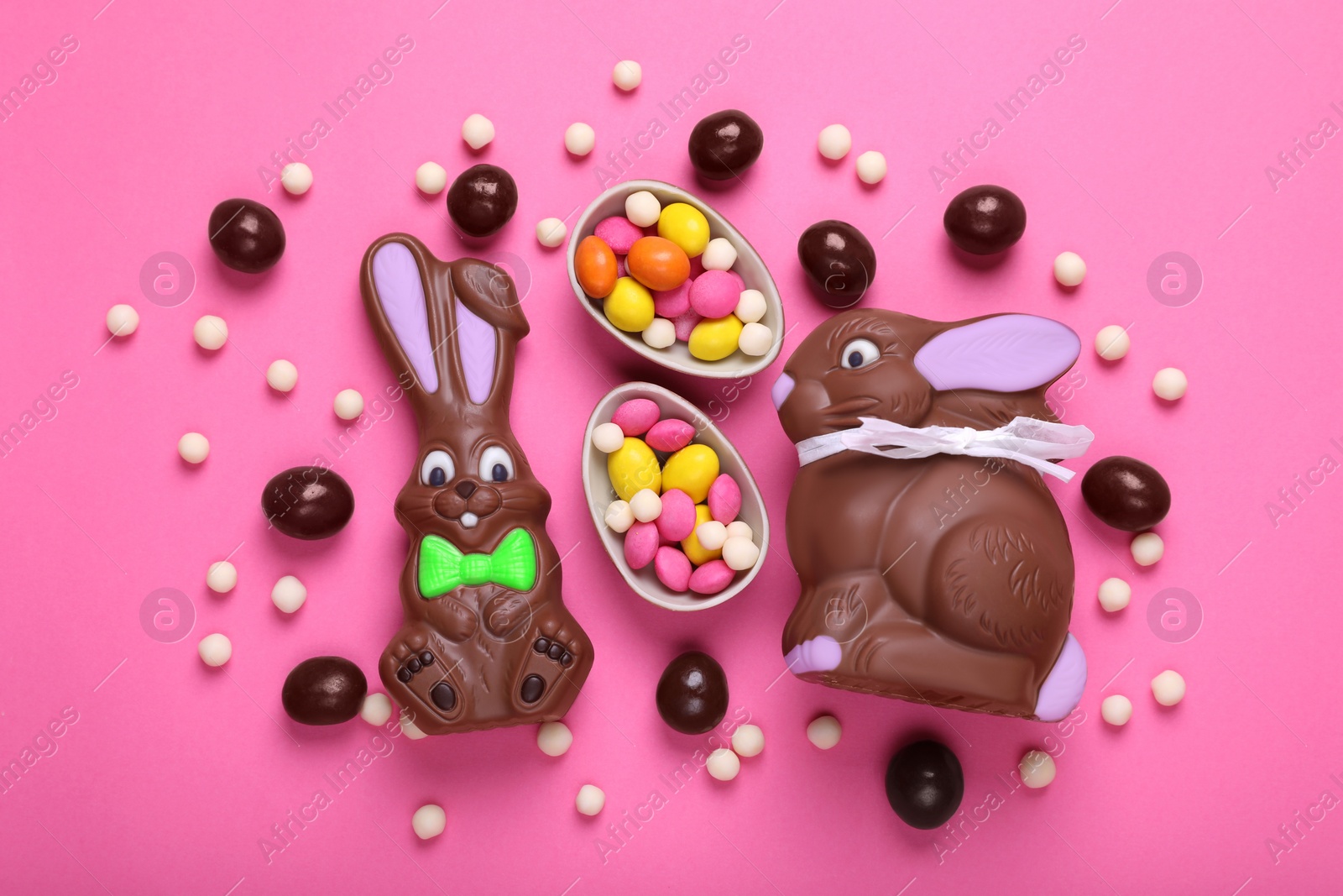 Photo of Chocolate Easter bunnies, halves of egg and candies on pink background, flat lay