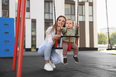 Happy nanny and cute little boy on swing outdoors