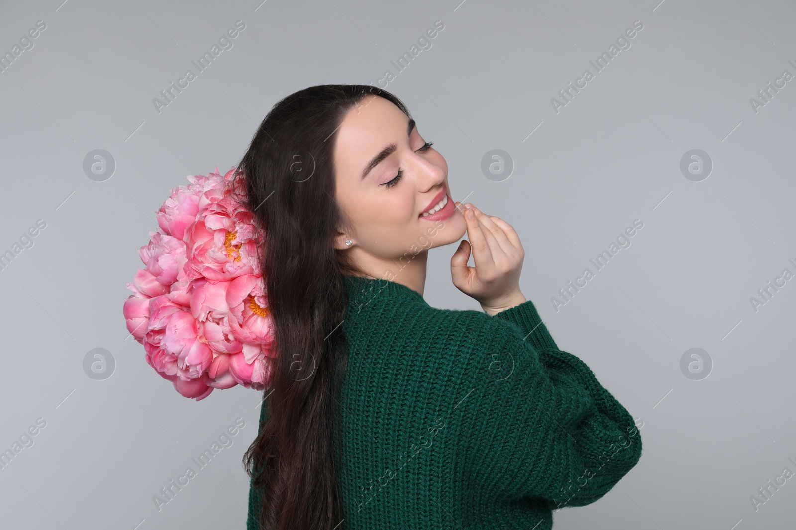 Photo of Beautiful young woman with bouquet of peonies on light grey background