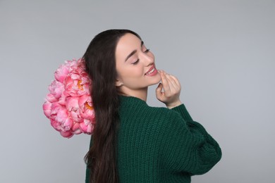 Photo of Beautiful young woman with bouquet of peonies on light grey background