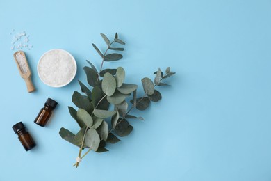 Aromatherapy products. Bottles of essential oil, sea salt and eucalyptus branches on light blue background, flat lay. Space for text