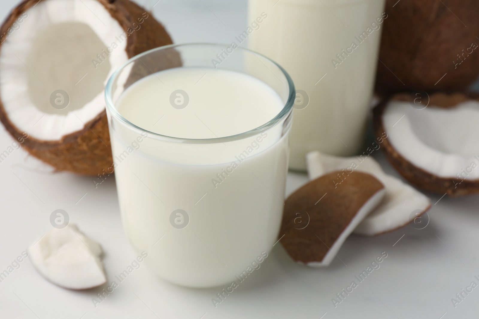 Photo of Glass of delicious vegan milk and coconuts on white table, closeup