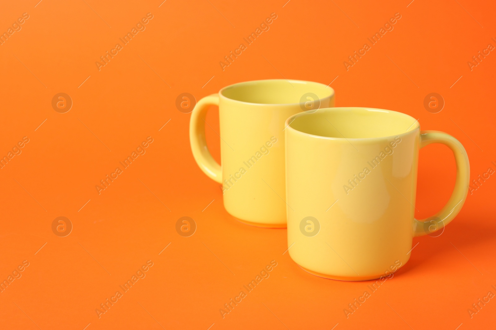 Photo of Two yellow ceramic mugs on orange background, space for text