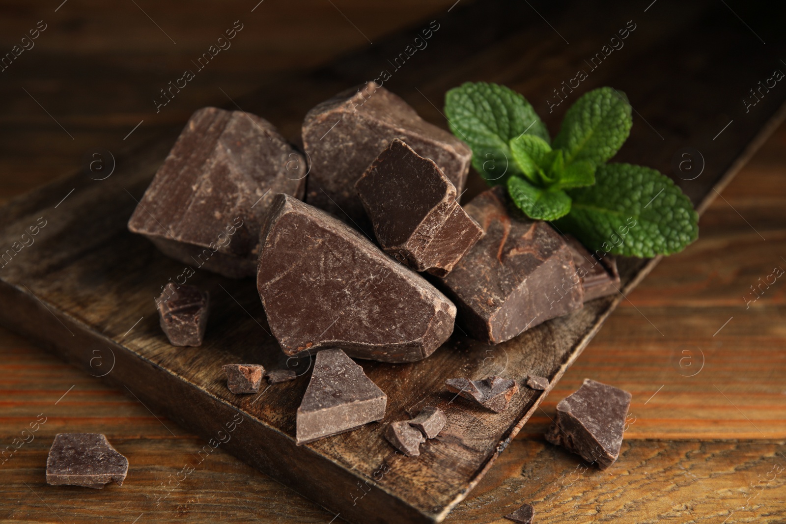 Photo of Tasty dark chocolate pieces with mint on wooden table