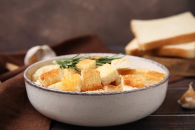 Photo of Delicious crispy croutons with rosemary in bowl on wooden table, closeup
