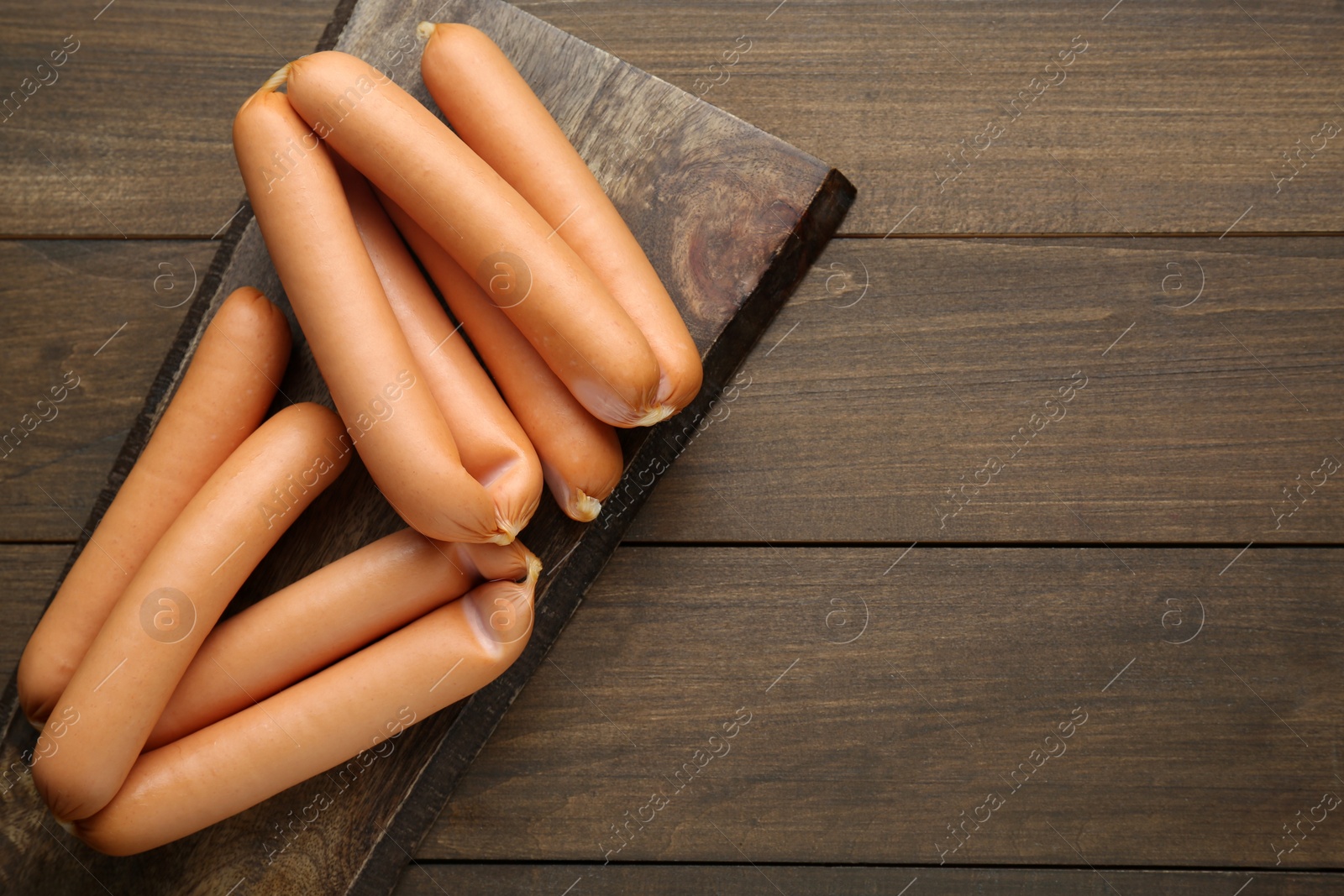 Photo of Delicious sausages on wooden table, top view. Space for text