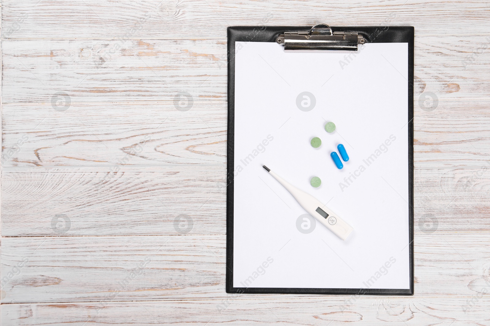 Photo of Clipboard, thermometer and pills on wooden table, top view. Space for text