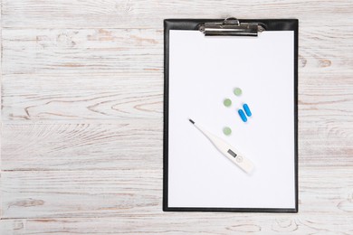 Clipboard, thermometer and pills on wooden table, top view. Space for text