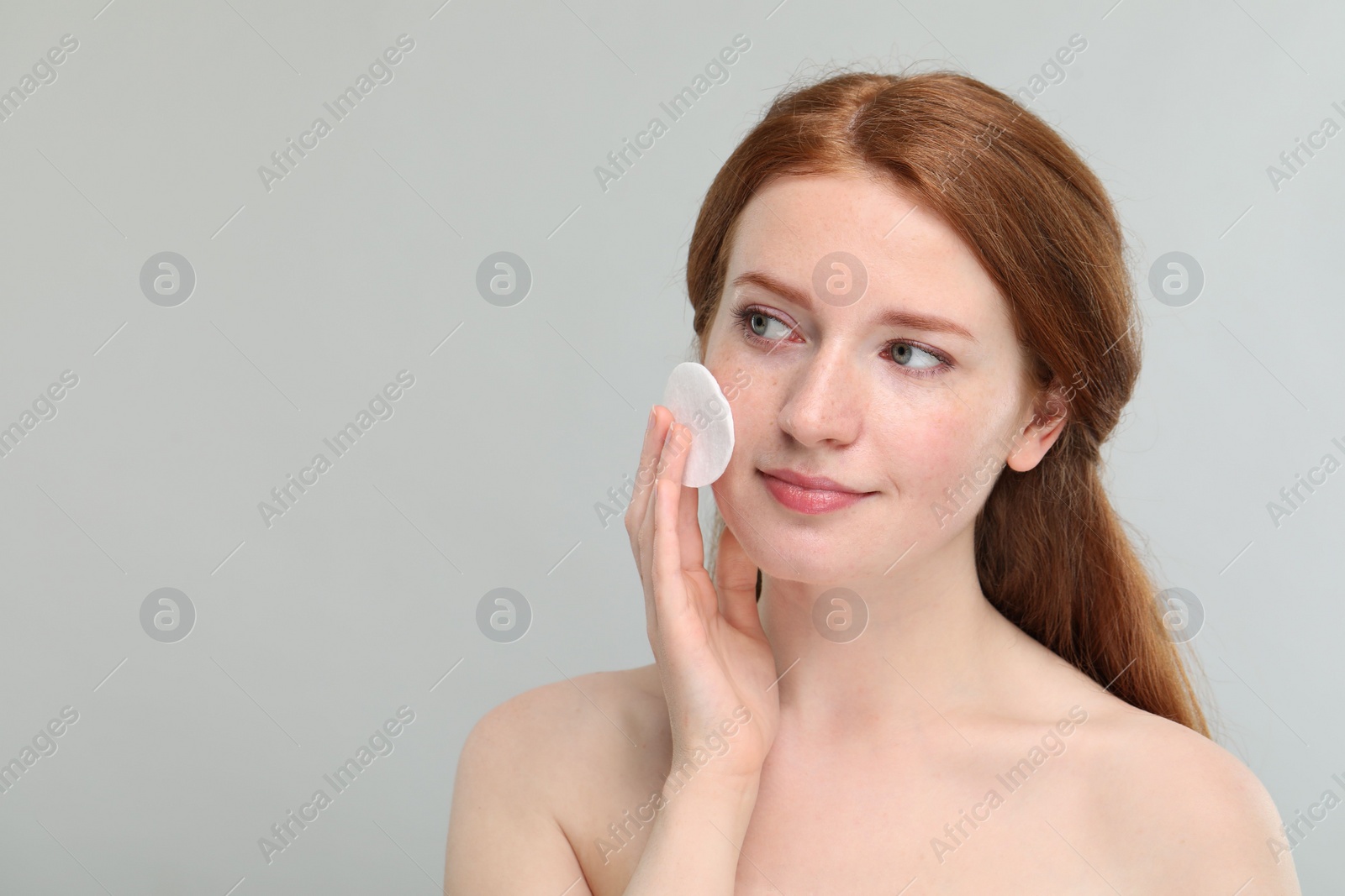 Photo of Beautiful woman with freckles wiping face on grey background. Space for text