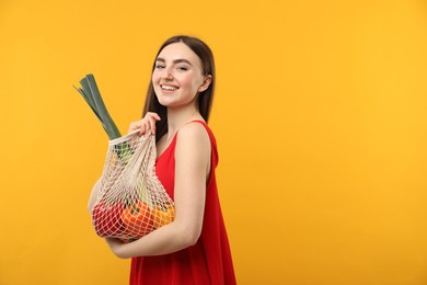 Photo of Woman with string bag of fresh vegetables on orange background, space for text