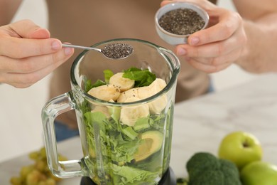 Photo of Man adding chia seeds into blender with ingredients for smoothie at table, closeup