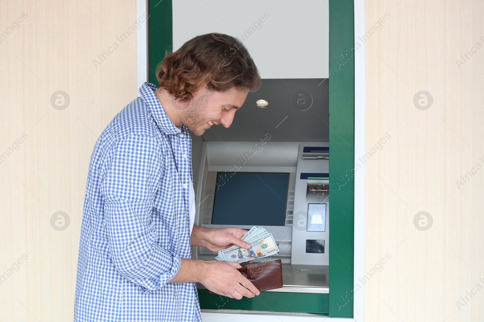 Photo of Young man with money near cash machine outdoors